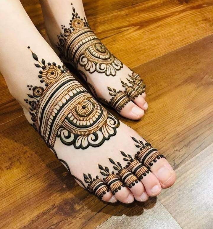 Feet with dark detailed mehndi featuring circular motifs, scalloped edges, bands and leafy details