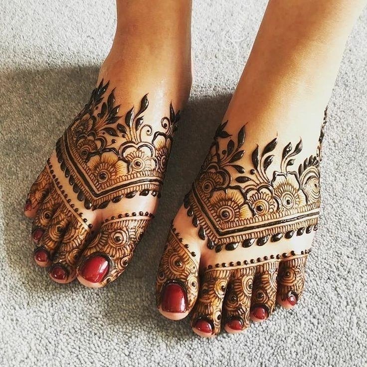 Feet with intricate dark mehndi bands, floral details and individually decorated toes with red toenail polish