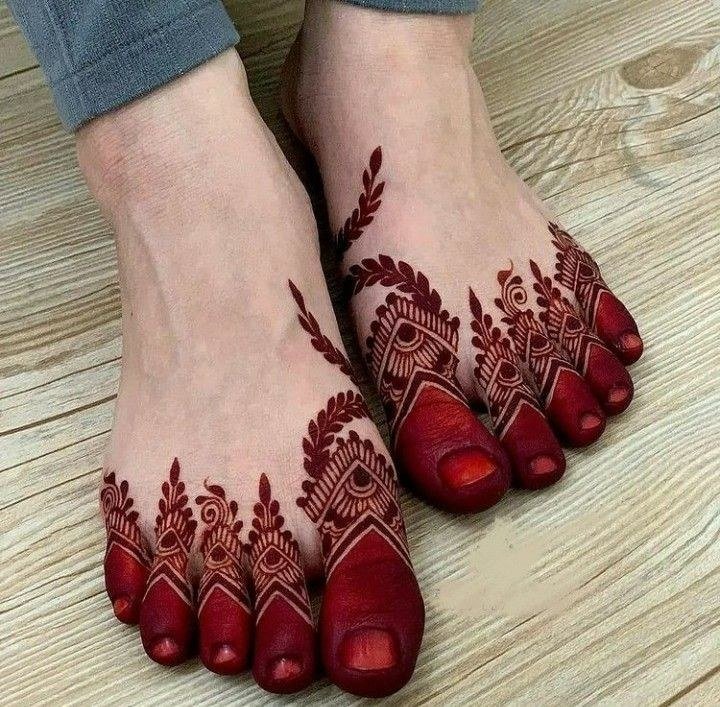 Feet covered with dark reddish mehndi featuring geometric toe details, floral shapes and leafy accents