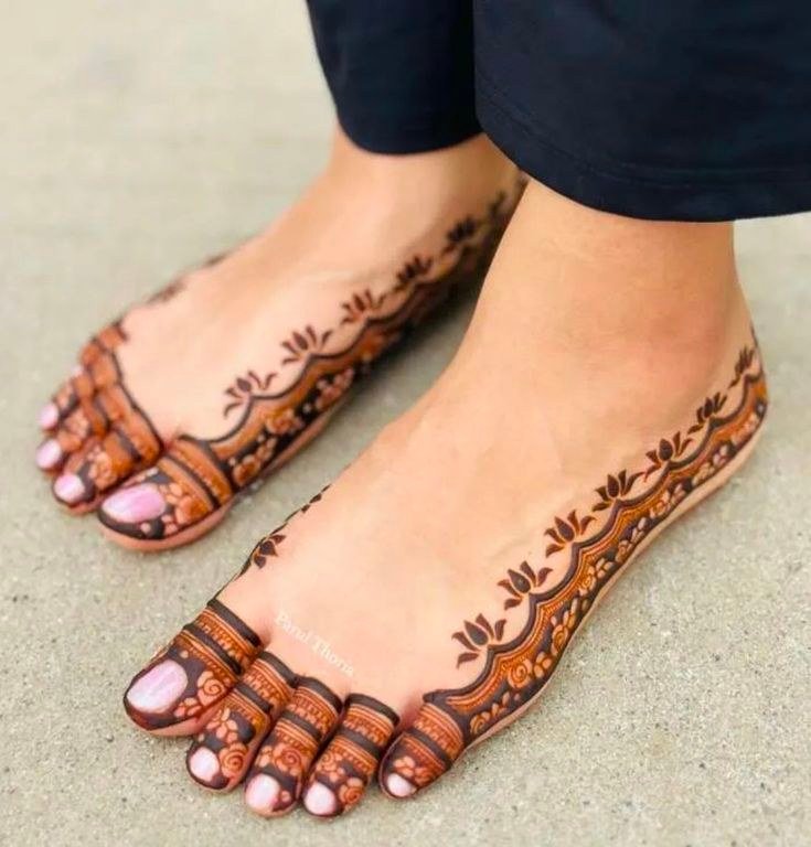 Feet with delicate reddish mehndi, decorated toes and thin leafy borders running along the sides