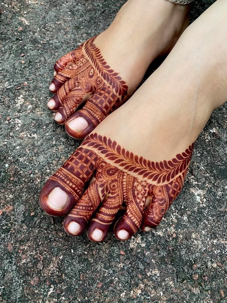 Feet with dark reddish mehndi featuring geometric bands, leafy borders and detailed toe patterns